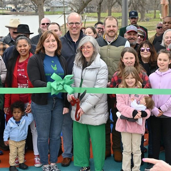 a large group of people standing behind a green ribbon ready to be cut