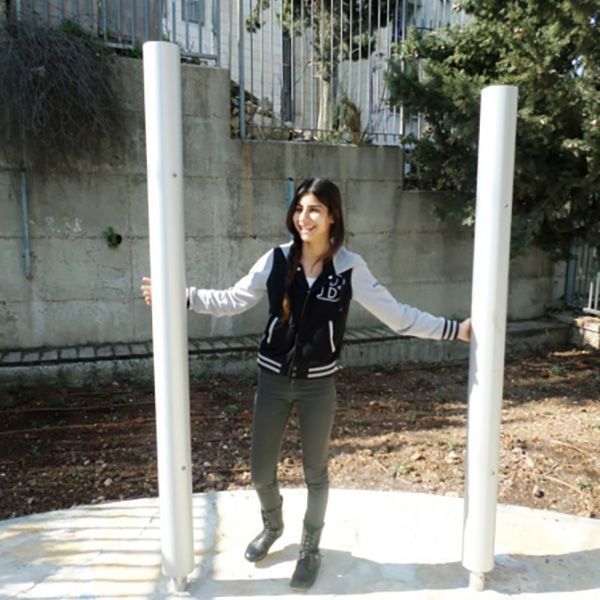 young girl with dark hair standing between two large musical chimes in playground