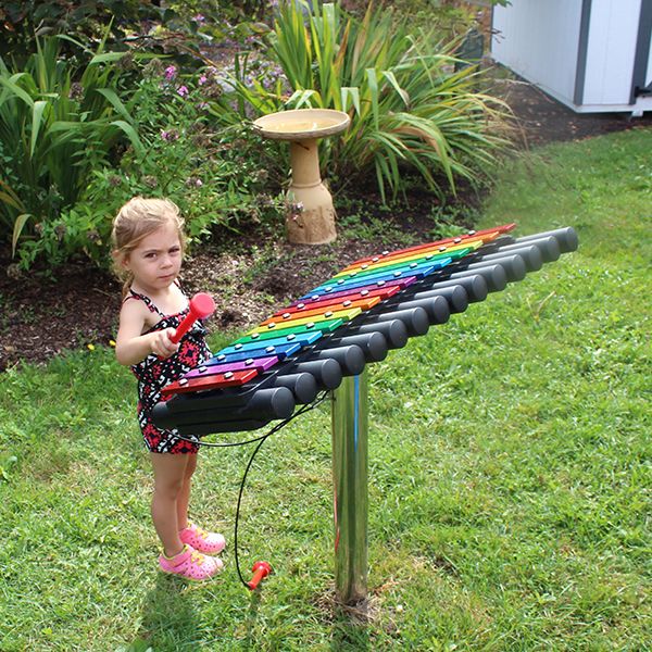 little girl playing the cavatina outdoor xylophone in the dino garden at Liverpool Public Library in New York