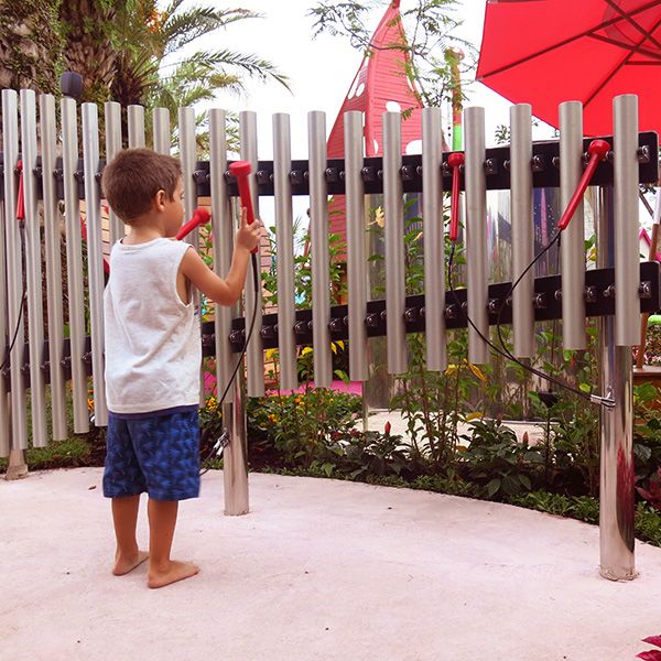 Little barefoot boy playing outdoor musical chimes in a playground in Brazil