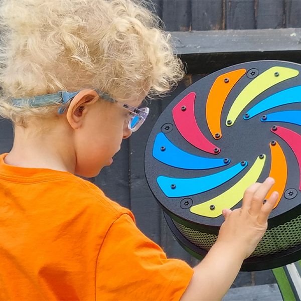 a young blond boy with special needs playing a small outdoor rain wheel with rainbow colored flashes on the front