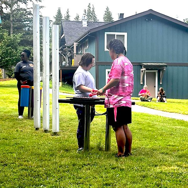 two girls playing on an outdoor xylophone in the camp beausite new musical garden