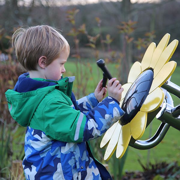 A young boy playing an outdoor musical drum in the shape and colours of a sunflower