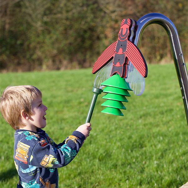 a young boy playing an outdoor musical instrument shaped like a firefly on a stainless steel post