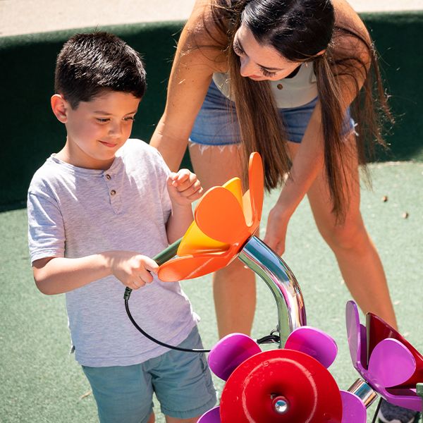 a young boy playing an outdoor musical flower with his mother a the sesame street music park at seaworld