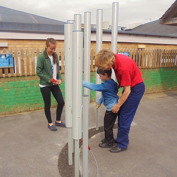 young boy and his carer playing large outdoor tubular bells together in special needs school playground