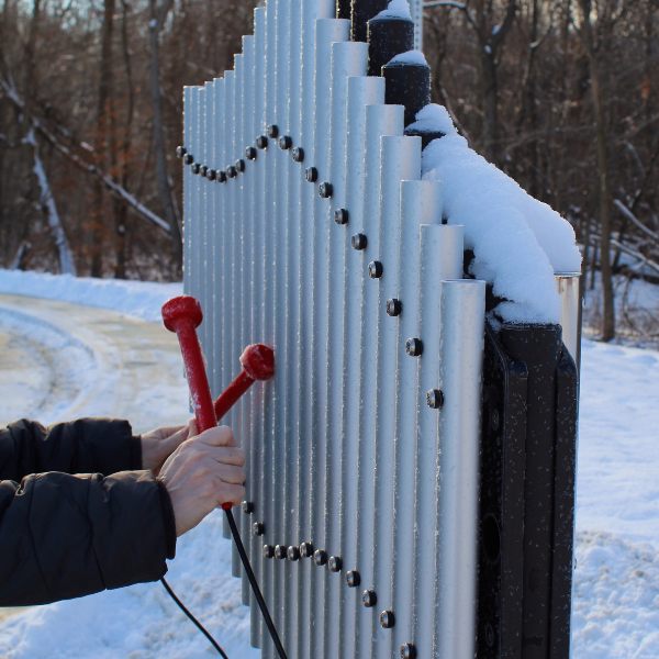 outdoor musical chimes covered in snow being played with a pair of red beaters