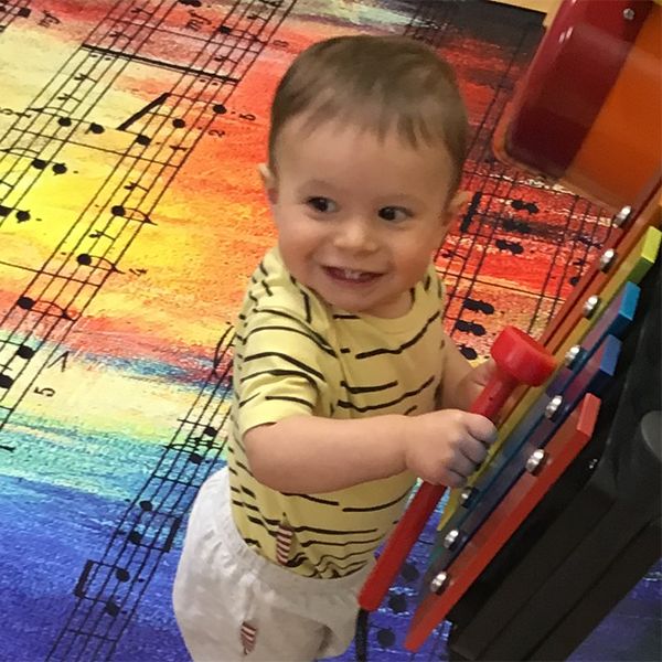 a young child playing a wall mounted rainbow coloured xylophone in their nursery school