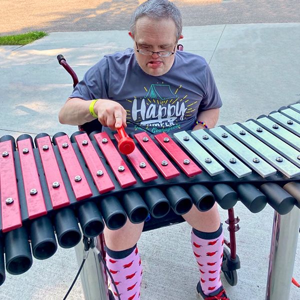 a man with special needs playing a dual colored outdoor xylophone in the camp courageous musical playground