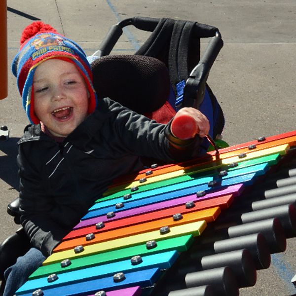 little boy in a wheelchair playing a rainbow coloured outdoor playground xylophone