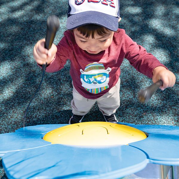 Little boy playing an outdoor drum shaped like a forget me not flower in an inclusive park 