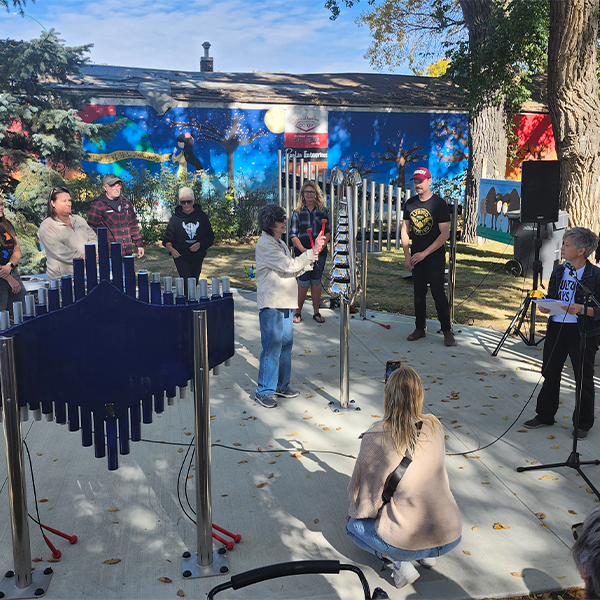 A performer plays an outdoor musical instrument surrounded by an audience in a vibrant outdoor setting with colorful murals.