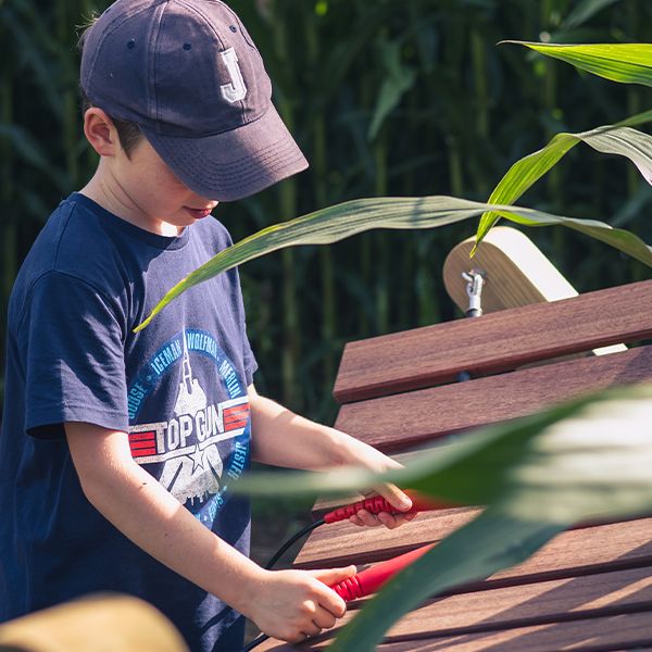 A large outdoor wooden xylophone being played by a young boy in a corn field