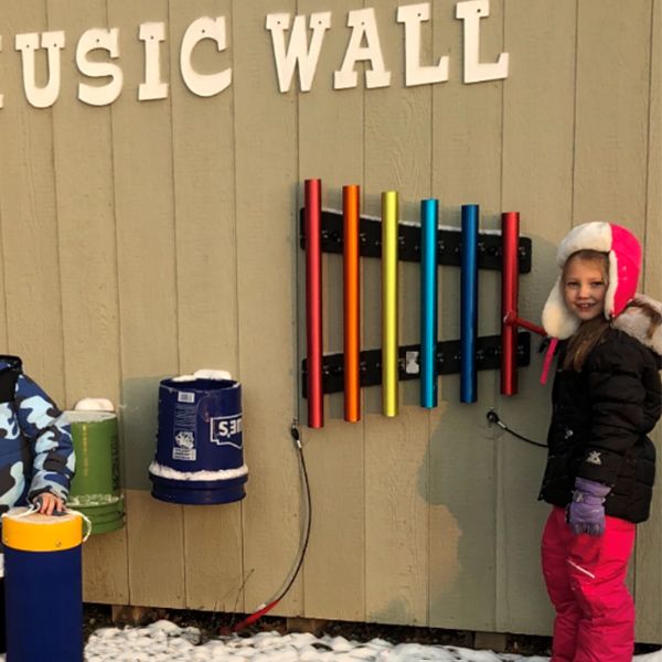 young girl in a christmas hat playing rainbow chimes on a wall