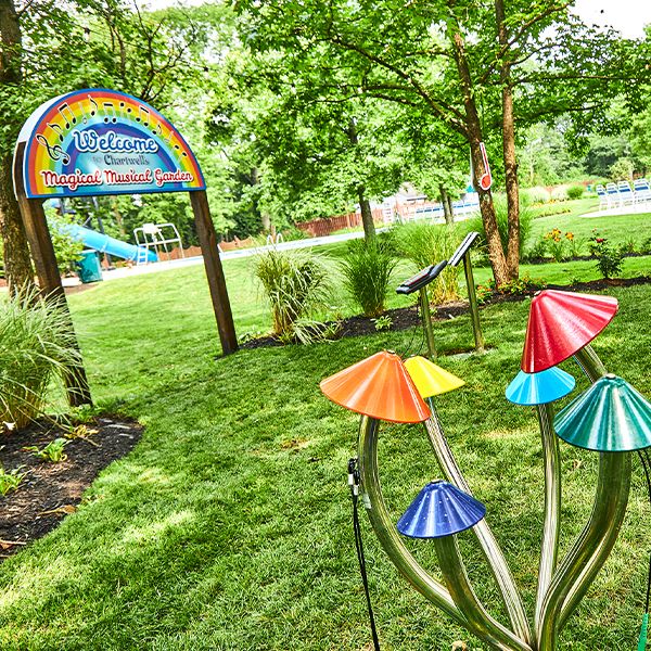 the sign to the Chartwell Happy Day Camp Musical Garden with a set of outdoor colourful musical chimes shaped like mushrooms in front