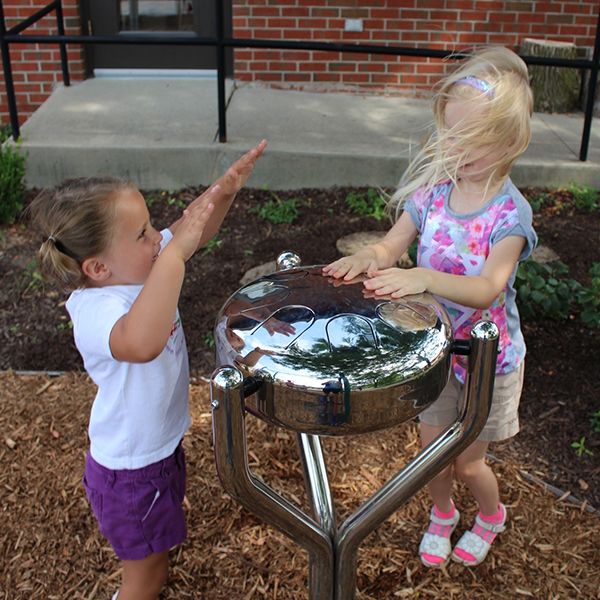 two girls playing a silver outdoor babel drum in the children's healing center garden