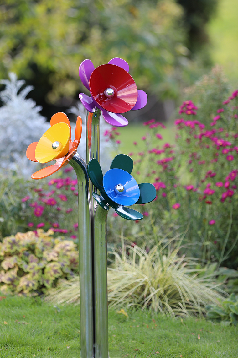 A posy of three flower shaped coloured musical bells on a stainless steel stand located outdoors in a meadow