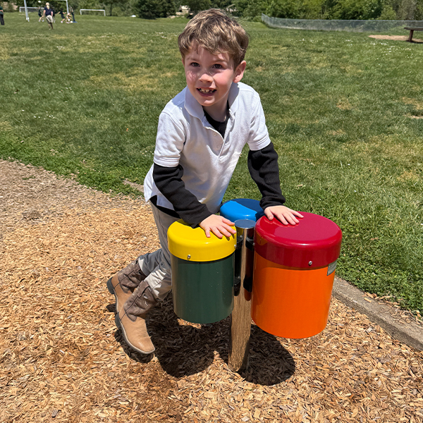 Young Boy playing a colorful set of  outdoor bongo drums in a school playground