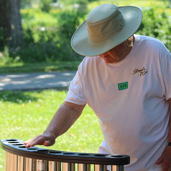 an older man wearing a hat playing an outdoor musical instrument called handpipes in the belleville rotary music garden