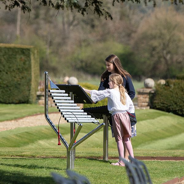 two ladies playing on an aluminum outdoor musical instrument within the grounds of north cadbury court