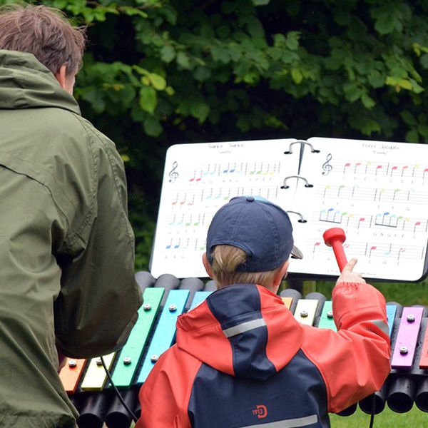 A father and son playing an outdoor xylophone with an outdoor music book