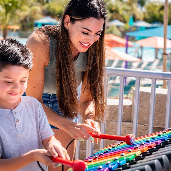 mother and child playing a rainbow colored outdoor xylophone in the sesame street music park at seaworld