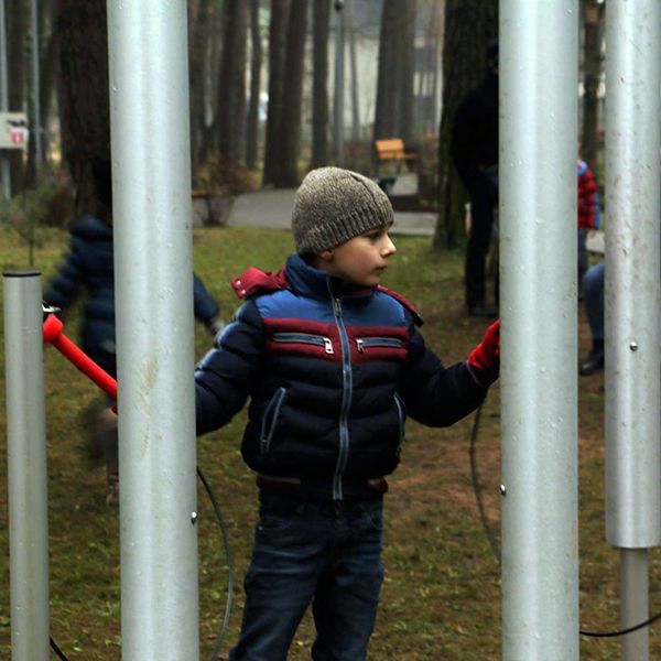 Little boy wearing a winter hat playing a large silver musical chime instrument in a park