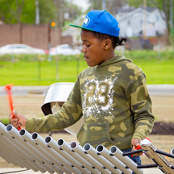 teenage boy wearing a blue cap playing a large silver outdoor musical instrument