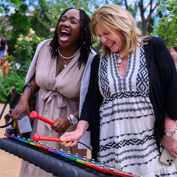 two ladies wearing lanyards laughing while playing a colourful outdoor xylophone