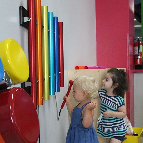 two little girls playing on rainbow coloured musical instruments on the wall at the building for kids childrens museum