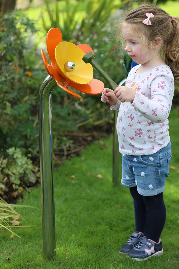 a young girl playing a yellow and orange musical flower outdoors in a sensory garden