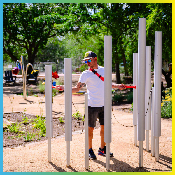 man playing large silver outdoor chimes using red mallets in an outdoor music space