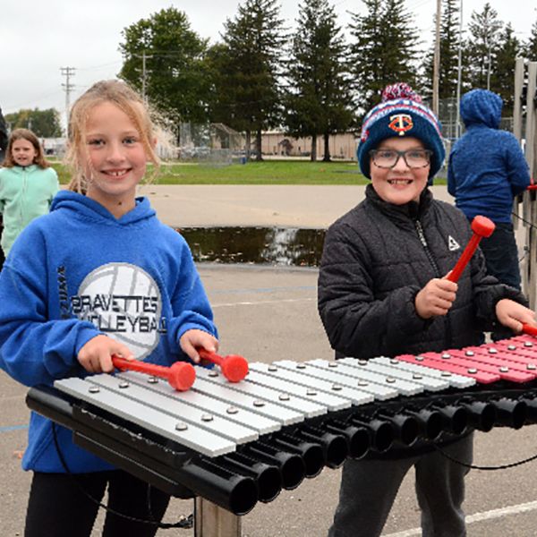 two young girls playing a large outdoor xylophone in an elementary school playground