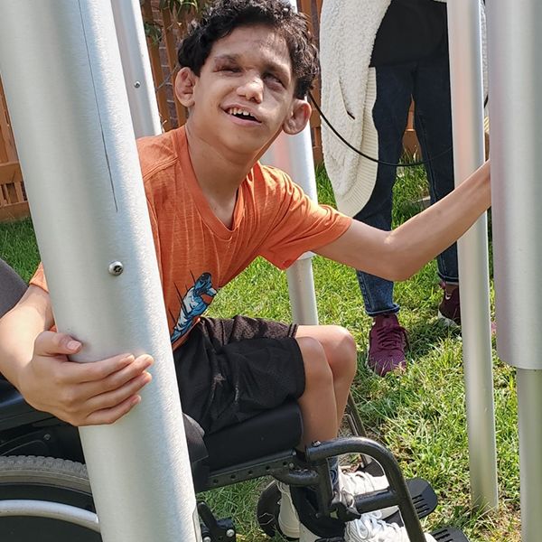 a young blind boy in a wheel chair playing tubular bell outdoor musical instruments in a music garden