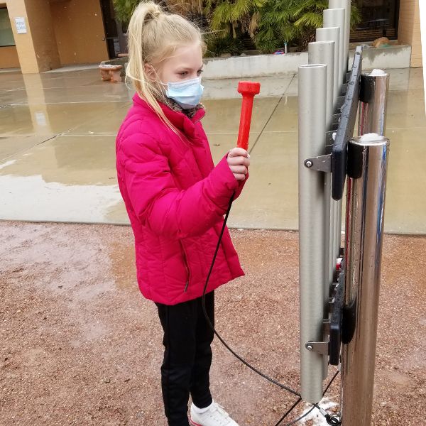 A schoolgirl wearing a red uniform playing an outdoor musical chimes in the school playground