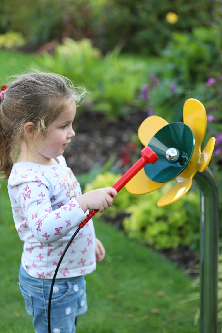 a young girl playing a yellow and green musical flower outdoors in a sensory garden