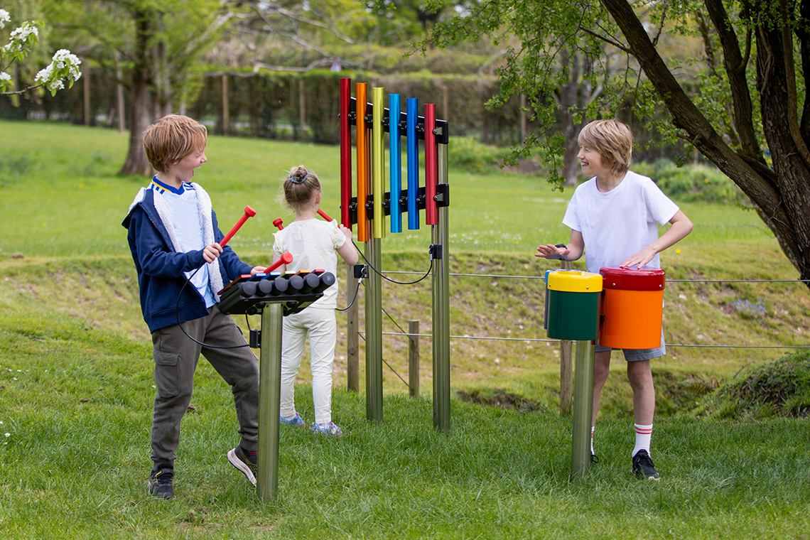 Group of children playing on three rainbow coloured outdoor musical instruments