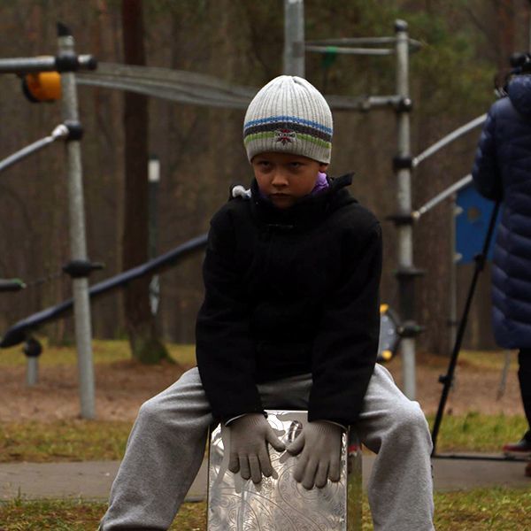 Boy dressed for cold weather sitting on a stainless steel cajon drum in a playground