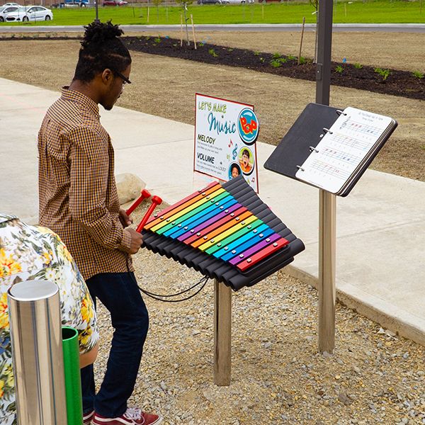 a young man playing a rainbow colored outdoor xylophone and music book at the dayton metro library