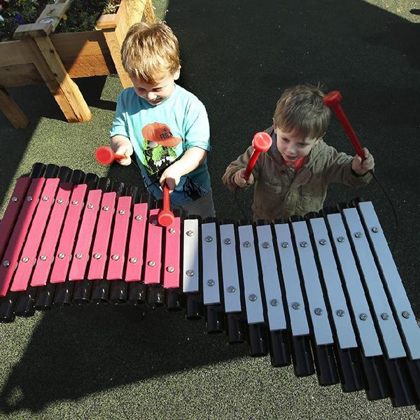 Little boy in a duffle coat playing a pink outdoor xylophone in Little Rock Zoo Sensory Garden