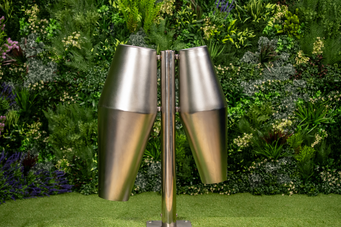 Pair of stainless steel outdoor drums mounted on a single post on a lush green artificial turf. The background features a vibrant vertical garden with various plants.