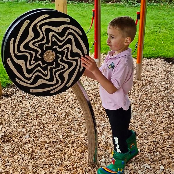 A young man with autism happily playing on a large circular black and silver rainwheel at the Thomas Centre