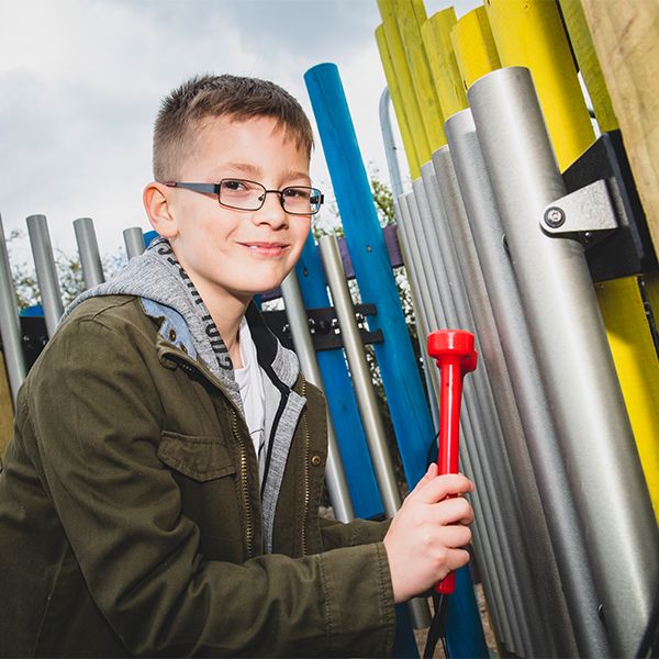 boy wearing glasses and winter coat playing the musical chimes in the music maze at national adventure forest