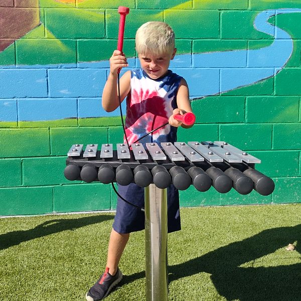 a young boy playing an outdoor xylophone with red mallets at the musical garden in town of versailles