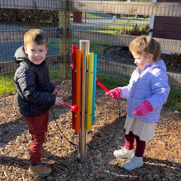 a young boy and girl playing a rainbow coloured outdoor musical chimes post