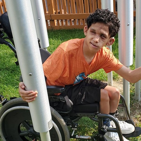 a young blind boy in a wheel chair playing tubular bell outdoor musical instruments in a music garden