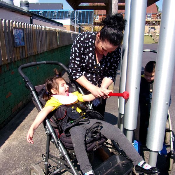 young girl and her carer playing a stainless steel outdoor tongue drum together in special needs school playground