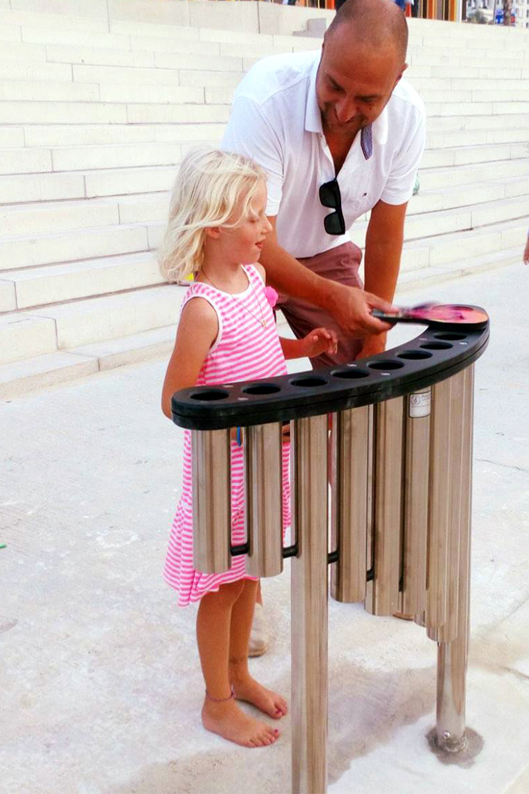 Father and daughter playing on a set of handpipes outdoor musical instrument on the side of the beach in Tel Aviv