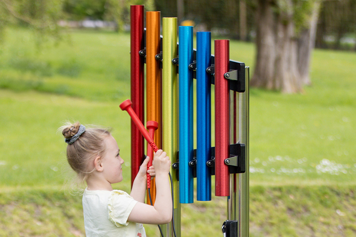 a set of bright rainbow coloured pentatonic chimes played by young girl in the outdoors