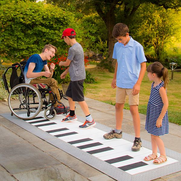 four children including one in a wheelchair playing on a giant outdoor floor piano